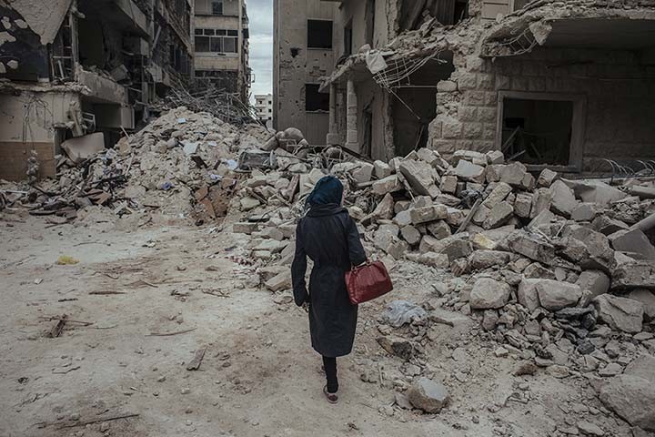 Une jeune femme marche dans les dŽcombres juste aprs qu'une bombe "baril", larguŽe par le rŽgime, ait explosŽ dans le quartier de Saif Al-deawla, au sud ouest d'Alep, SYRIE 03/05/2015 Durant toute la durŽe de mon reportage a Alep, je logeais chez un soldat de l'ArmŽe Syrienne Libre. Nous Žtions quatre a vivre sous son toit. Le premier jour, alors que nous prenions notre petit dŽjeuner, (il Žtait 9h du matin) nous avons entendu des bombes exploser au loin puis nous avons entendu un Žnorme sifflement. Une bombe venait d'tre larguŽe au dessus de nous. Tout le monde a couru dans le cuisine pour tenter d'y trouver refuge. Je n'ai pas couru avec eux, je suis restŽ sans bouger en me disant que si la bombe devait tomber sur notre b‰timent, je ne pouvais pas Žchapper a une mort certaine. Apres un gros "boum", j'ai rŽalisŽ que la bombe n'Žtait pas tombŽe sur nous. En rŽalitŽ elle avait explosŽ 200 mtres plus loin, sur une Žcole. Plusieurs enfants sont morts dans cette explosion ce jour laÉ Apres cette explosion, j'ai du partir rapidement car j'avais rendez-vous dans la prison pour rencontrer les deux prisonniers afghans. Ce n'est qu'en revenant (5 heures plus tard) que j'ai vu cette jeune femme, comme une apparition. Elle semblait chercher quelqu'un dans les dŽcombres.