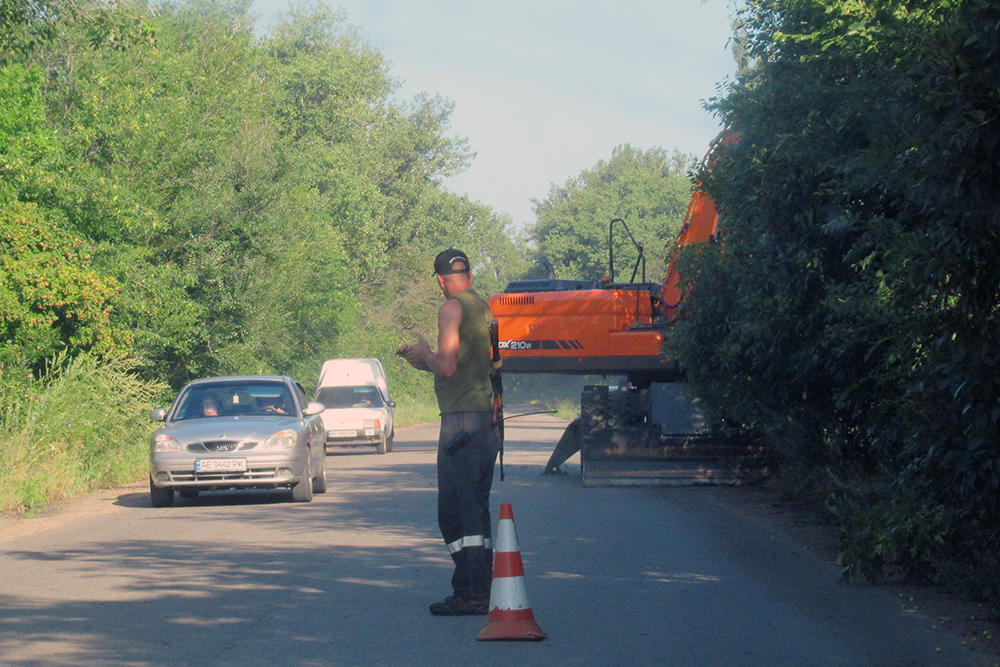 Le 15 juillet 2026, à Maryanske, entre Apostolove et Nikopol (oblast de Dnipropetrovsk), un homme chargé de la sécurité du chantier, équipé d'un détecteur de drones FPV et d'un fusil, surveille le passage des voitures tandis qu'un engin de travaux-