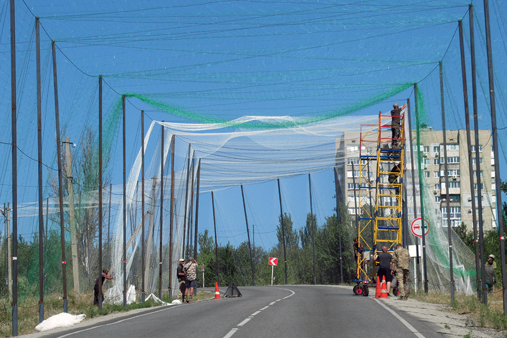 Le 13 août 2026, à la sortie de Baburka, au sud-ouest de Zaporizhia, des ouvriers installent un filet au-dessus de la route T0806 qui mène à Bilenke car les frappes de drone FPV y sont de plus en plus fréquentes. Photographie Thierry Birrer.