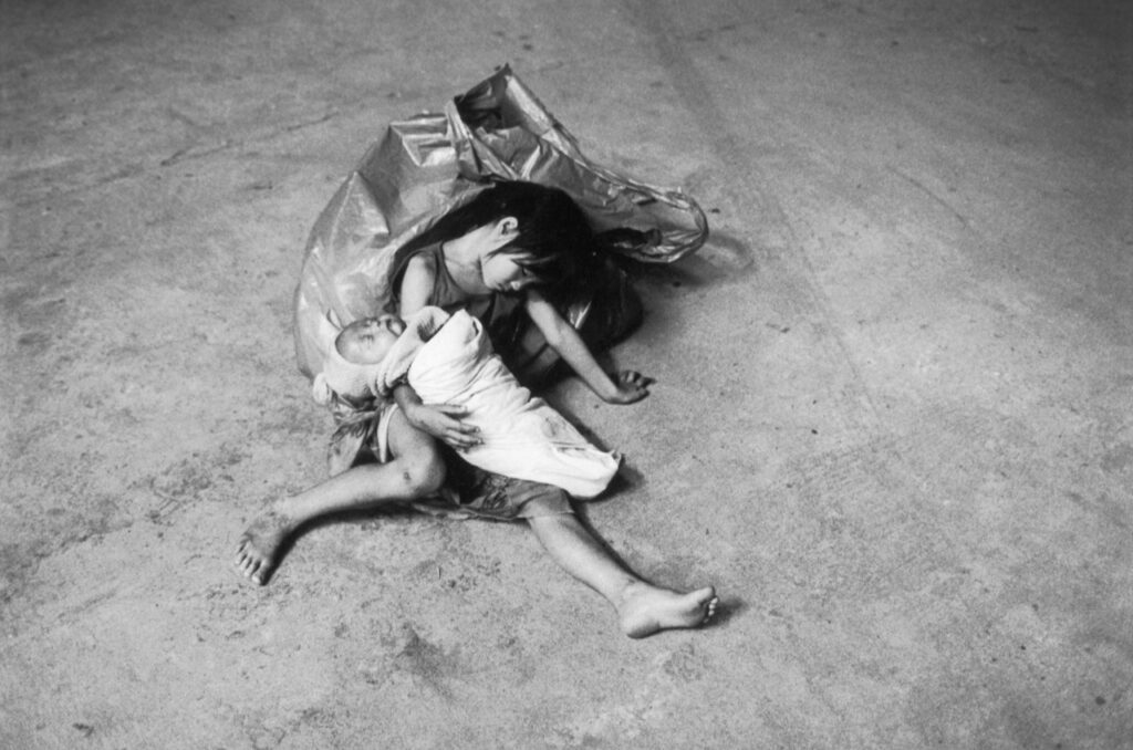La Petite Pietà. Vientiane, Laos. 2003 Elle avait tout au plus cinq ans. Ce n’était pas une mendiante mais une petite chiffonnière qui avait rempli toute la journée son sac de guenilles, de cannettes de soda et de bouteilles de bière. Elle s’était endormie là, épuisée, sur le trottoir dans la lumière d’un magasin encore ouvert à cette heure tardive. Elle tenait contre elle un bébé emmailloté qui dormait aussi, comme si c’était son bébé à elle. J’ai fait une photo, une seule. Je ne voulais pas la réveiller. Puis, je suis parti à pas de loup, m’enfuyant loin de cette petite endormie, si jeune et si vieille en même temps.Texte et photographie François Le Diascorn