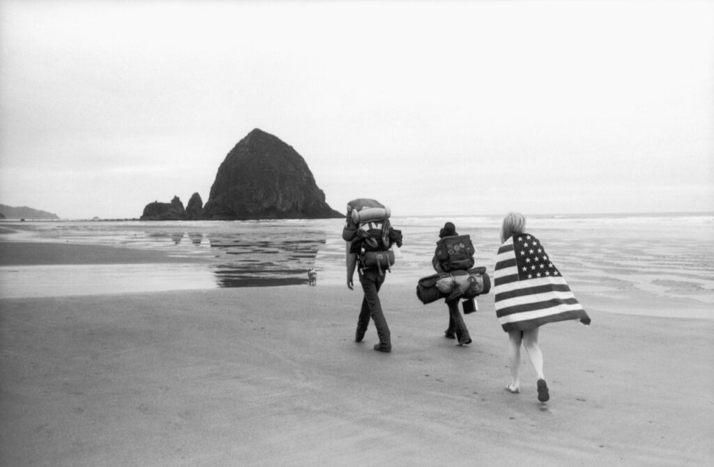 ) Les Marcheurs. Cannon Beach, Oregon, USA. 1976Il y a deux manières de photographier. Soit utiliser son imagination, faire des mises en scène ou bien refuser d’intervenir sur le réel, ne rester qu’un témoin passif. J’ai toujours préféré cette deuxième manière. Ou presque. En 1976, j’ai abandonné un travail bien payé comme commercial d’une agence de publicité prestigieuse, pour franchir le pas et devenir photographe à temps plein. J’ai choisi mon sujet : le drapeau américain. C’est le bicentenaire des États-Unis et les célébrations donneront lieu à un déploiement sans précédent de drapeaux. Je le sais et je vais entreprendre une série sur ce thème. Toutes les images seront faites sur le vif. Mais pas celle-ci. Je demande à Nancy de revêtir par-dessus son maillot la bannière étoilée (qui appartenait à son père) et de se promener le long de la plage de Cannon Beach en Oregon (l’État où elle a grandi). Je fais plusieurs photos mais, évènement imprévu, deux campeurs surgis de nulle part viennent s’interposer entre elle et le rocher au moment où un coup de vent donne au drapeau la même forme en pain de sucre que le rocher. Alors, mise en scène ou pas? A vous de décider.<br> Texte et photographie François Le Diascorn